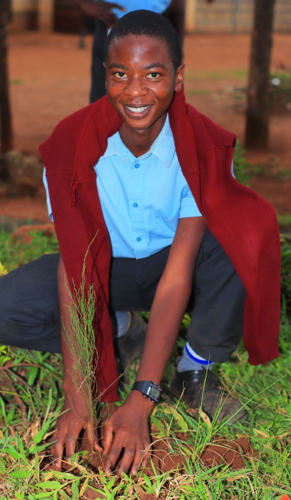 Two youth planting seedlings side by side in Kenya